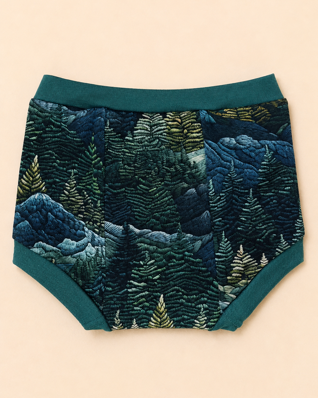 A pair of baby boy shorts featuring a detailed embroidered forest pattern in shades of blue, green, and beige, with solid teal green trim.
