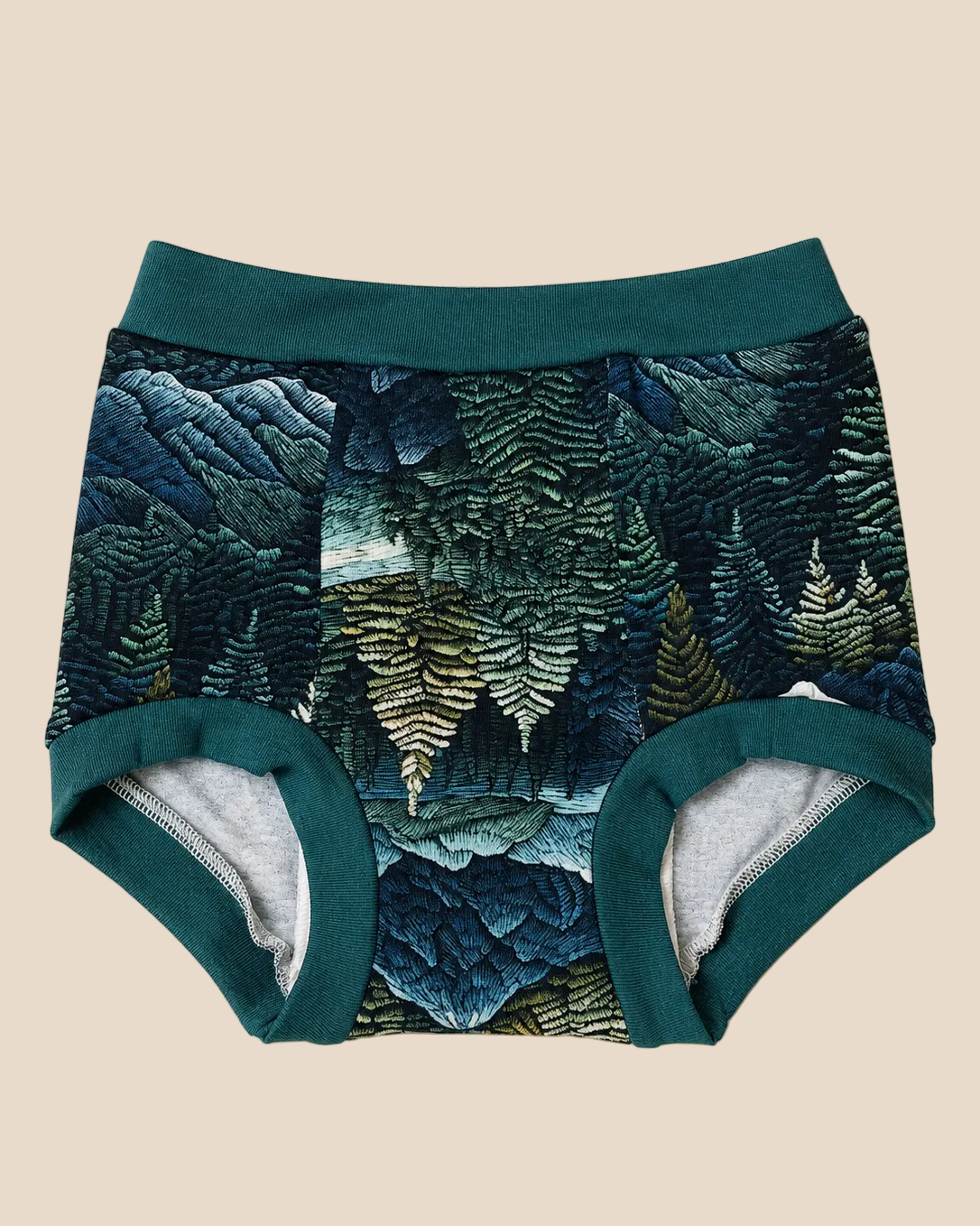 A pair of baby boyshorts featuring a dark teal and forest green fern forest pattern on the exterior, with solid dark teal trim and a light gray heathered interior lining, laid flat on a warm beige background.