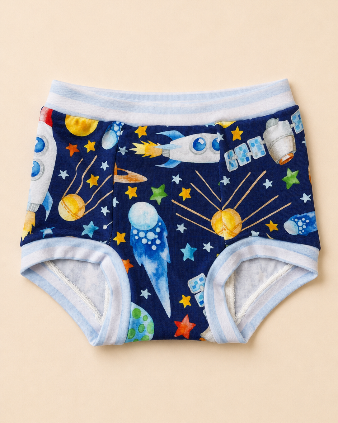 A pair of baby boy shorts with a colorful space-themed print on a navy blue background, featuring illustrations of rockets, planets, stars, and a rocket ship. The shorts have light blue and white striped trim and are displayed flat against a solid beige background.