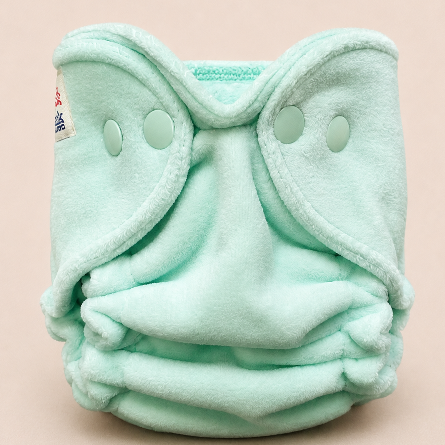 A mint green fleece reusable cloth diaper with snap closures, photographed against a solid pale pink background.