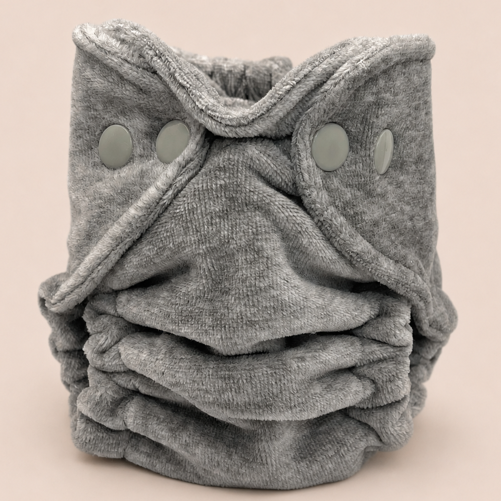 A folded gray reusable cloth diaper with three snap closures, photographed on a solid light beige background.
