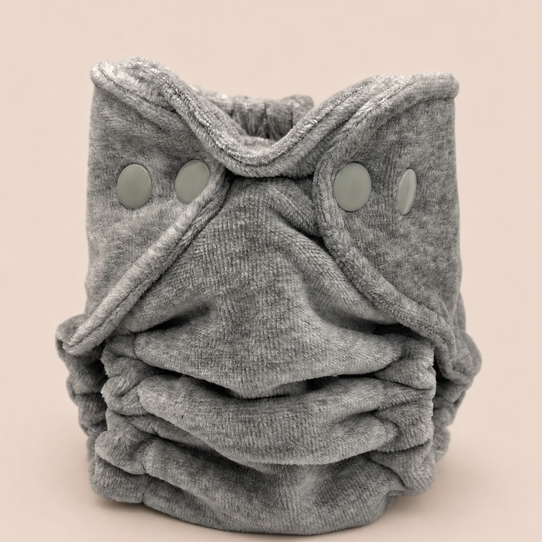 A folded gray reusable cloth diaper with three snap closures, photographed on a solid light beige background.