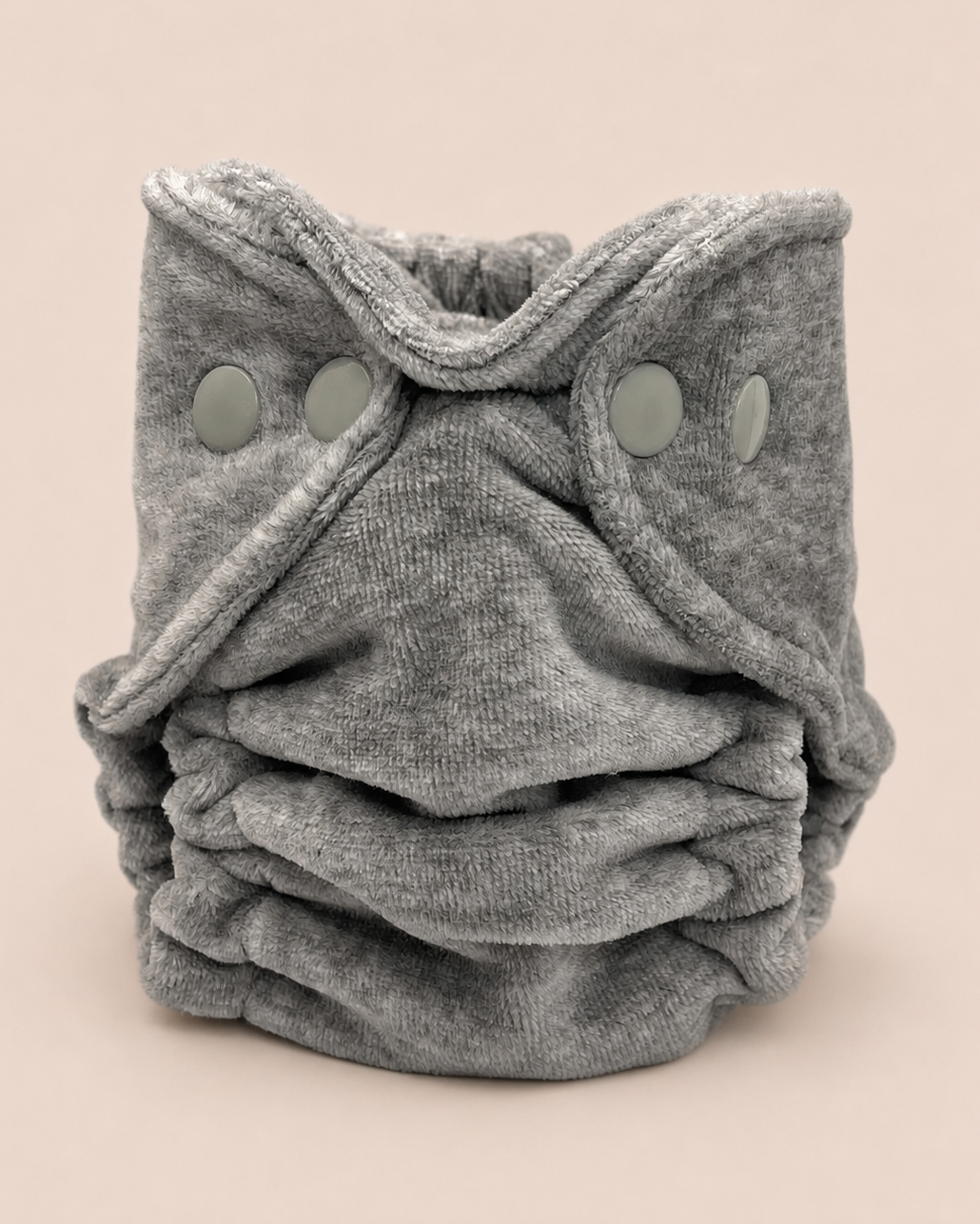 A folded gray reusable cloth diaper with three snap closures, photographed on a solid light beige background.