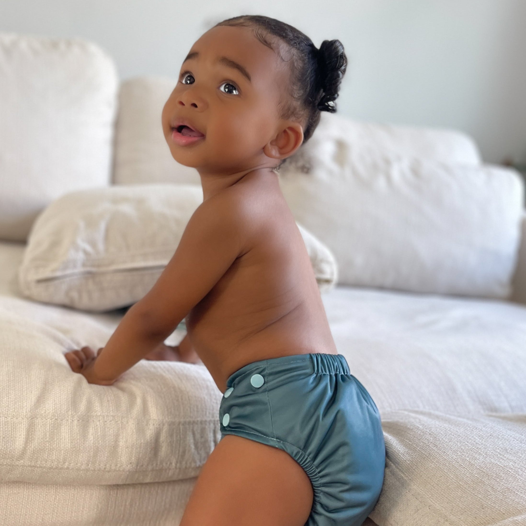 Child wearing a blue diaper sitting on a beige couch.