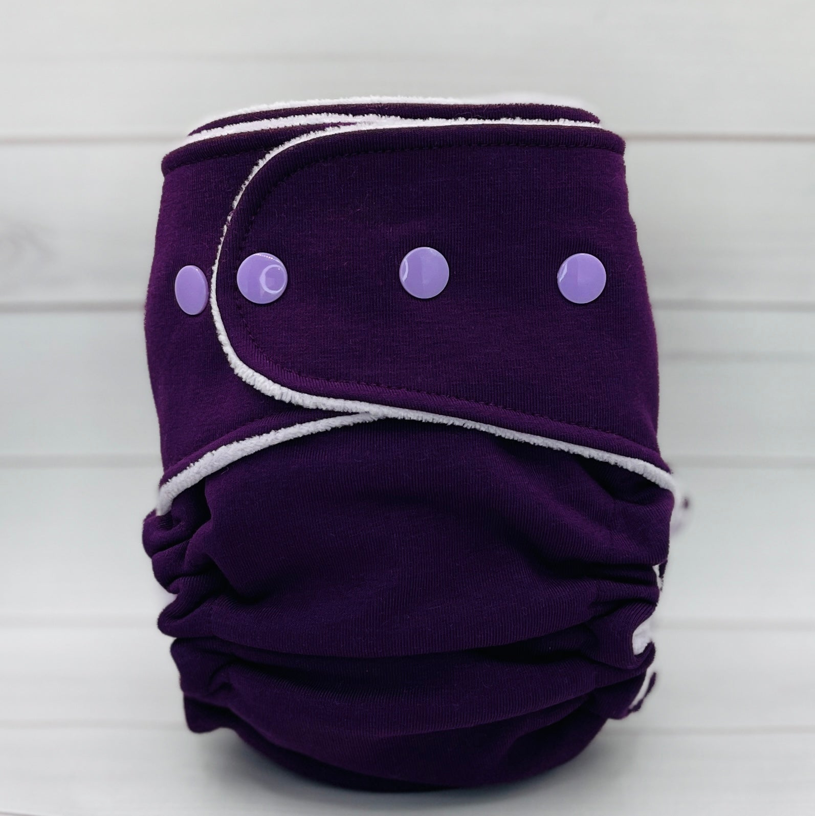 Purple cloth diaper with white trim and purple buttons on a white background
