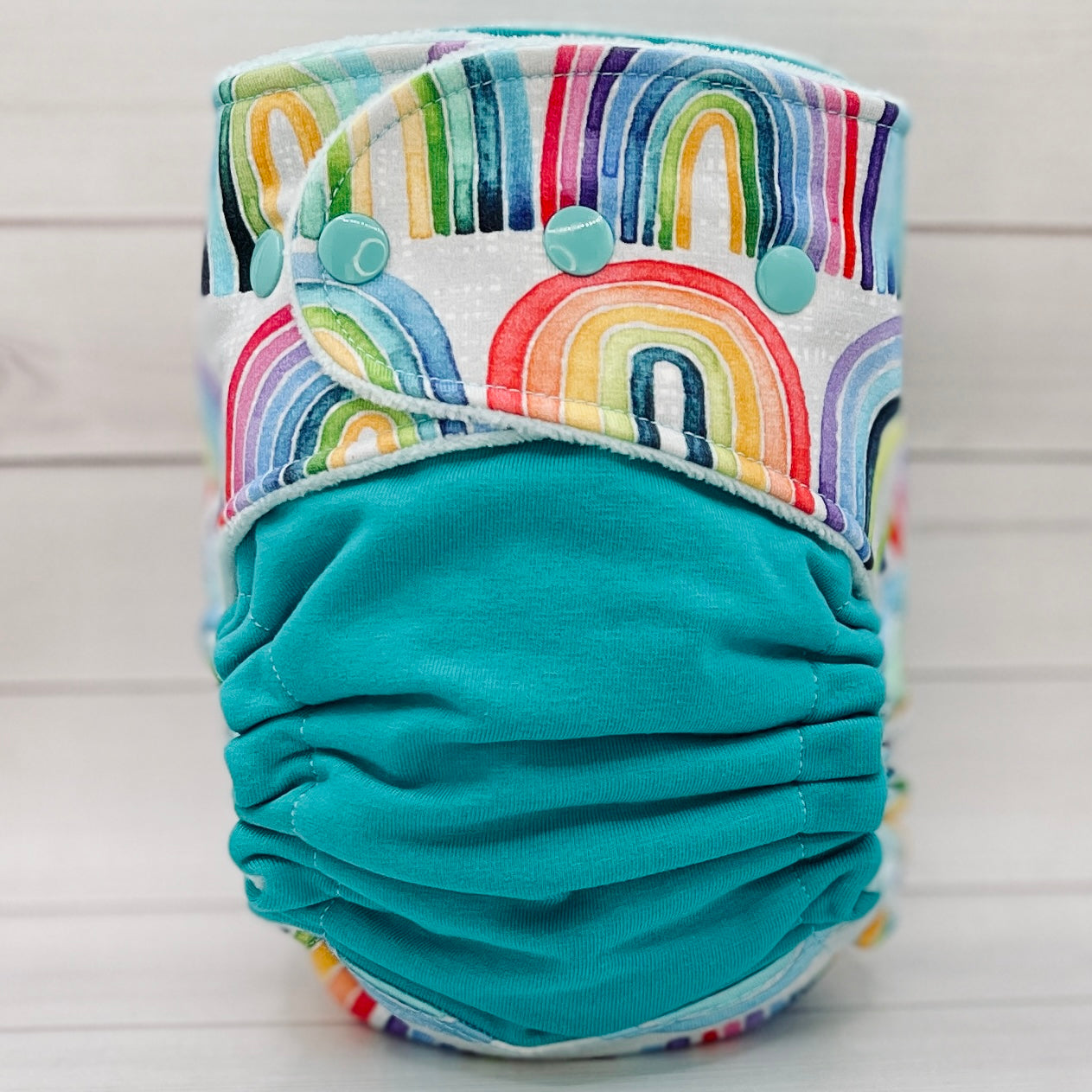 Turquoise cloth diaper with colorful rainbow pattern on a light wooden background