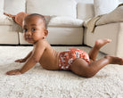 Baby in a diaper with a pattern on a carpeted floor in a living room.