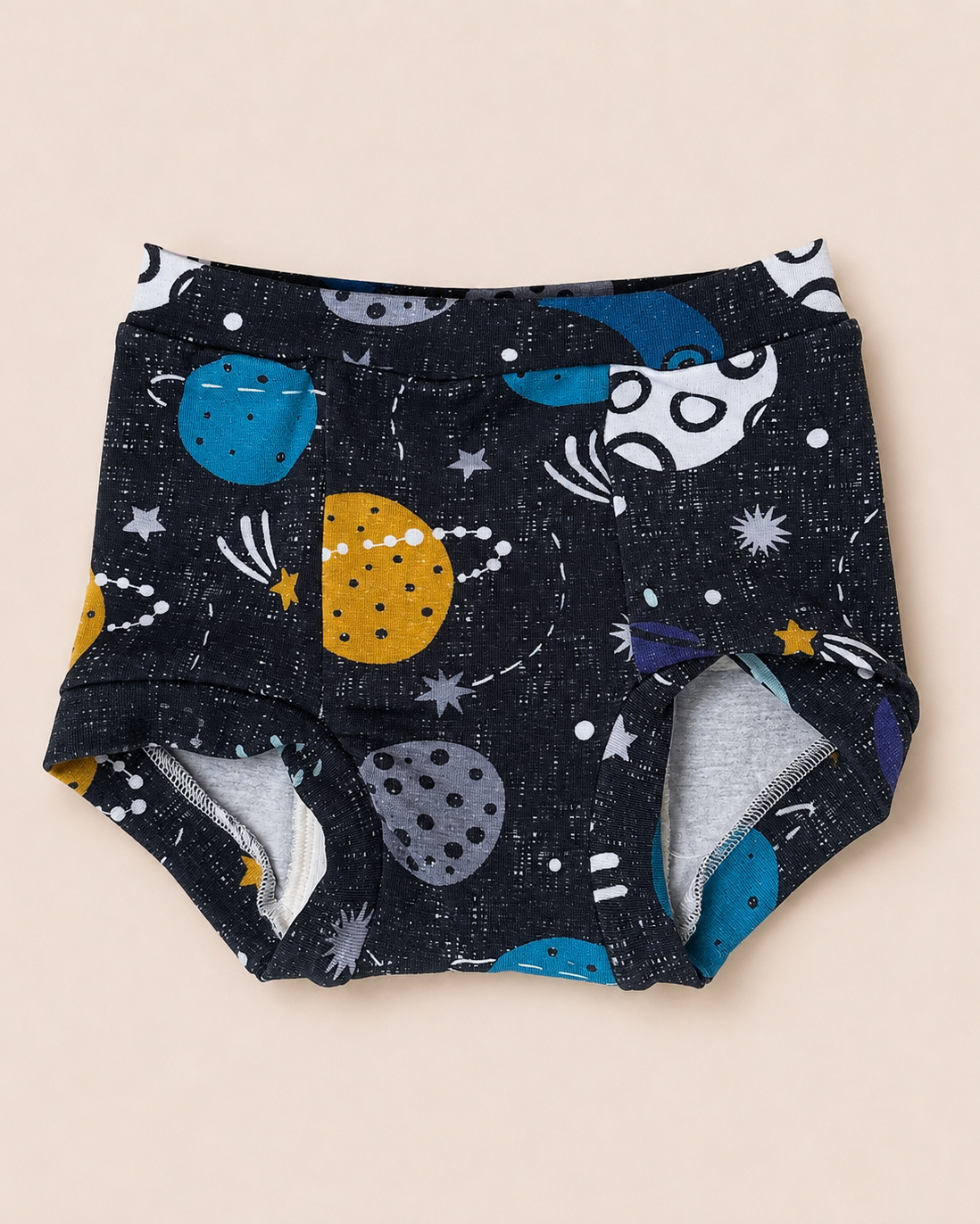 A pair of baby trainers with a dark navy blue space-themed print featuring colorful planets, stars, and comets, laid flat on a light beige background.