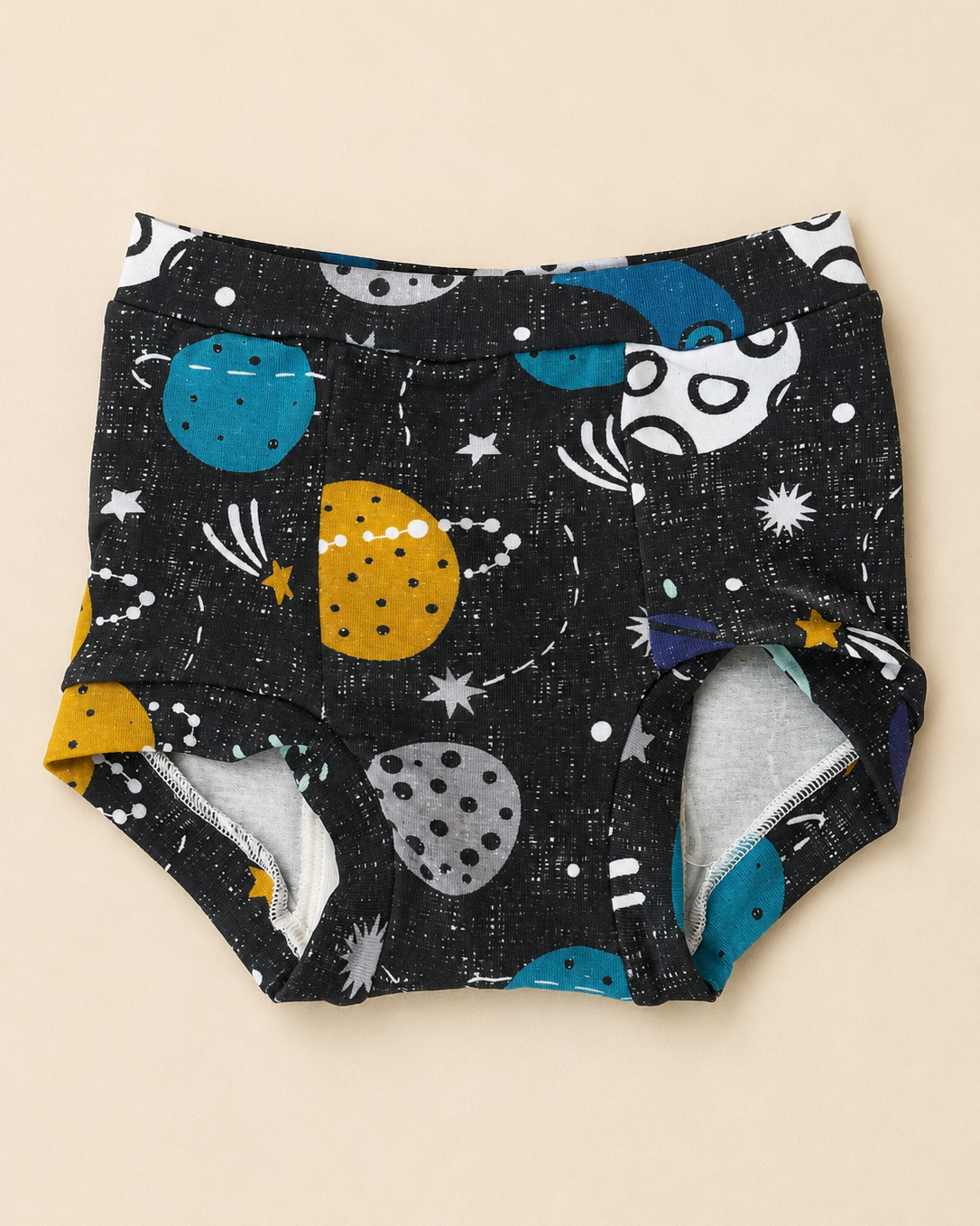 A pair of training underwear in a black space-themed print with colorful planets, stars, and rockets, shown flat on a light beige background.