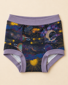 A pair of children's briefs with a purple waistband and leg cuffs, featuring a colorful cosmic print with planets, stars, and a crescent moon on a dark background, laid flat on a light beige surface.