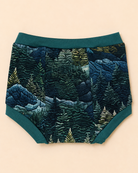 A pair of baby boy shorts featuring a detailed embroidered forest pattern in shades of blue, green, and beige, with solid teal green trim.