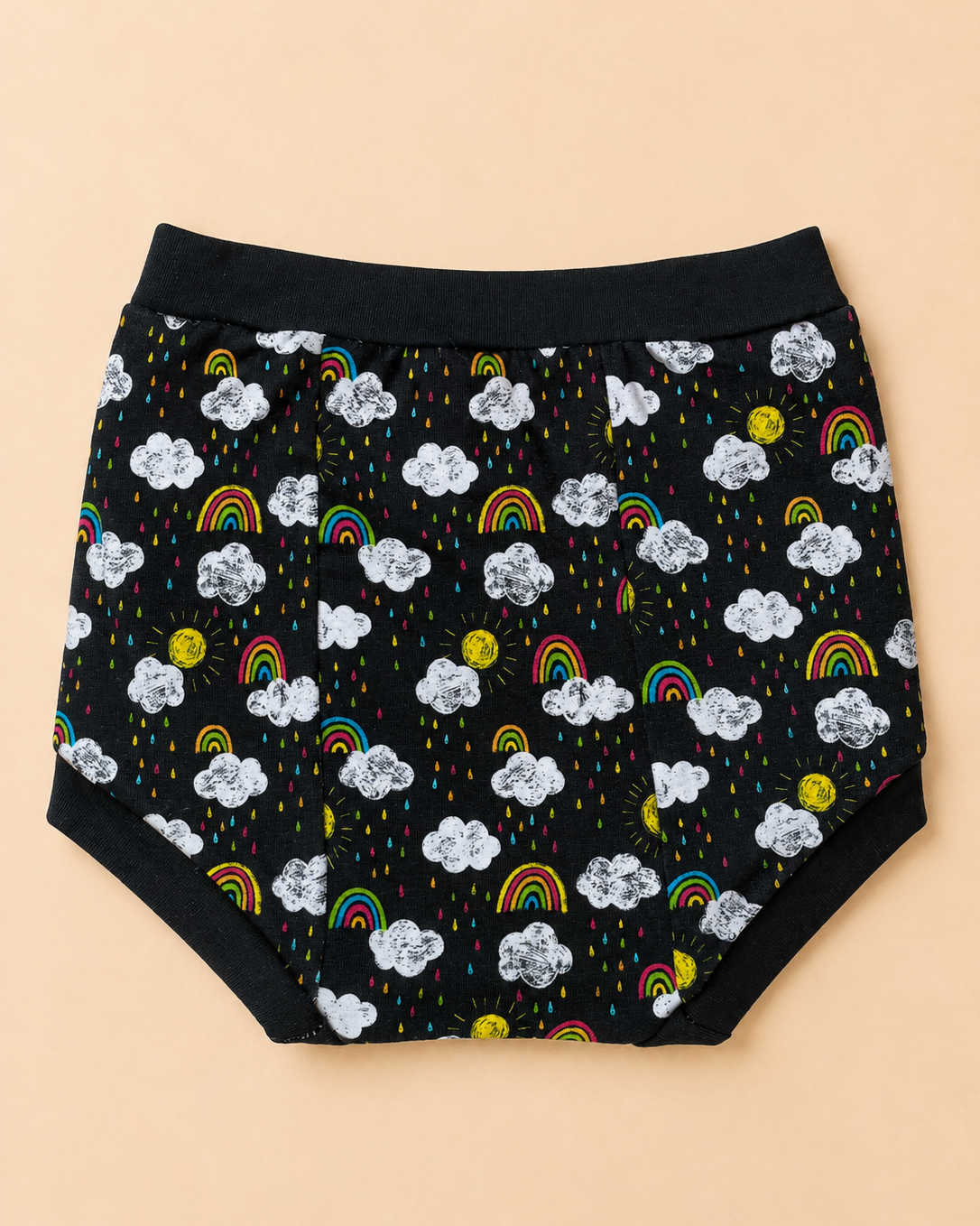 Black diaper cover with a playful cloud, rainbow, and sun print, laid flat on a solid beige background.