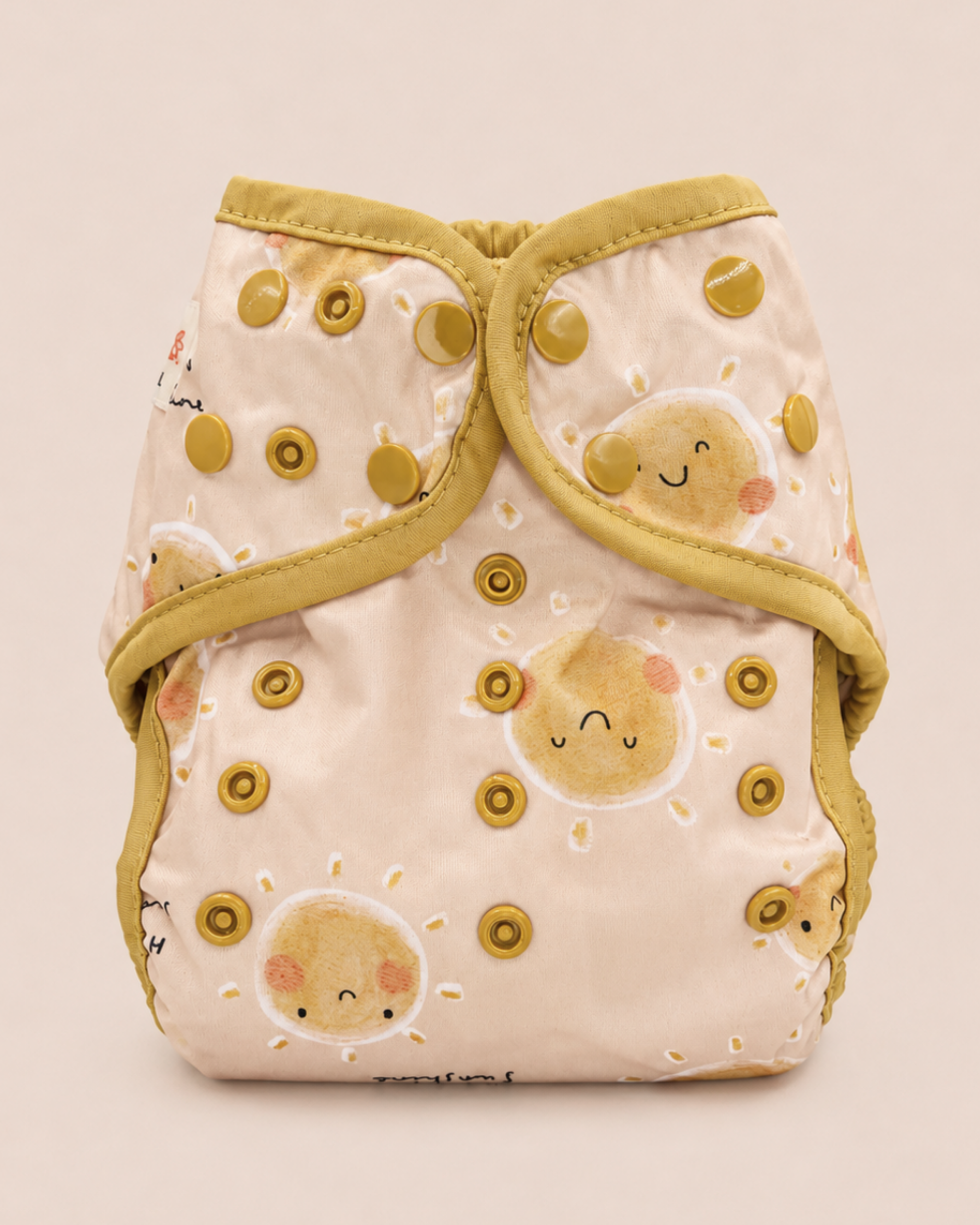 A reusable cloth diaper with a pale pink background, decorated with a pattern of smiling sun faces and olive green trim, shown against a solid light beige background.