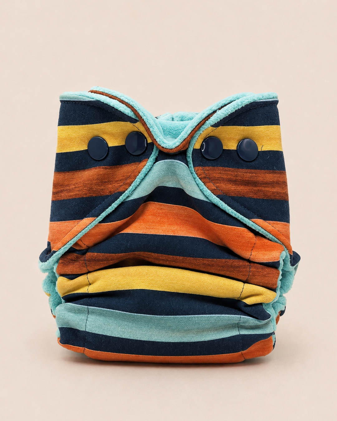 A striped reusable cloth diaper with a colorful pattern of navy, orange, yellow, and turquoise stripes, featuring three dark snap buttons on the front, set against a solid beige background.