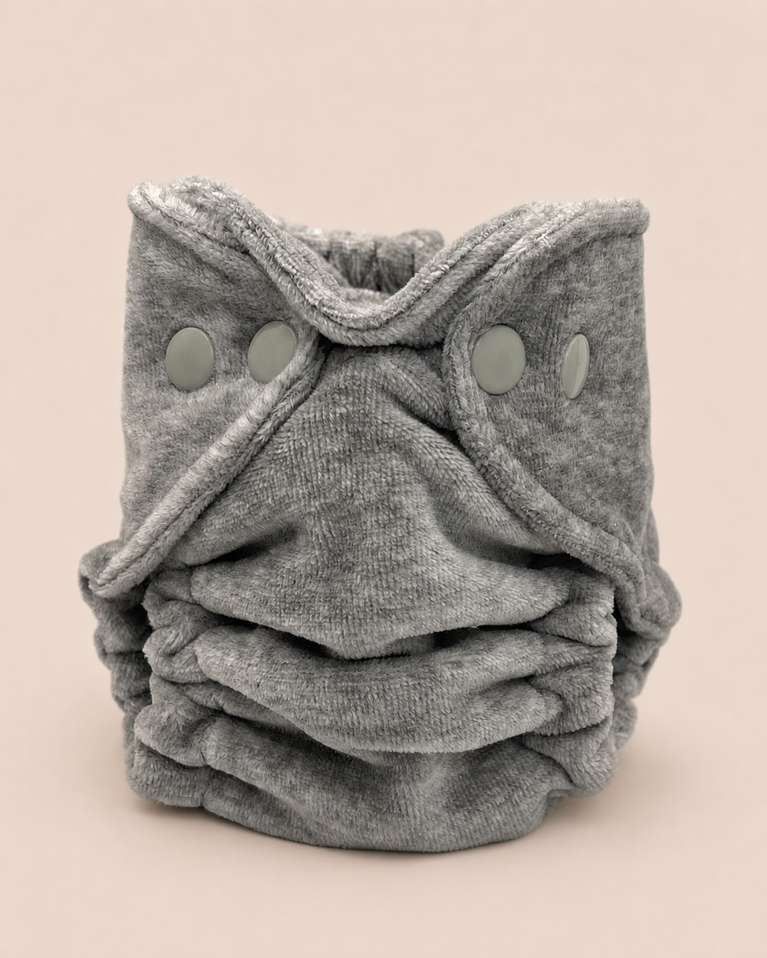 A folded gray reusable cloth diaper with three snap closures, photographed on a solid light beige background.
