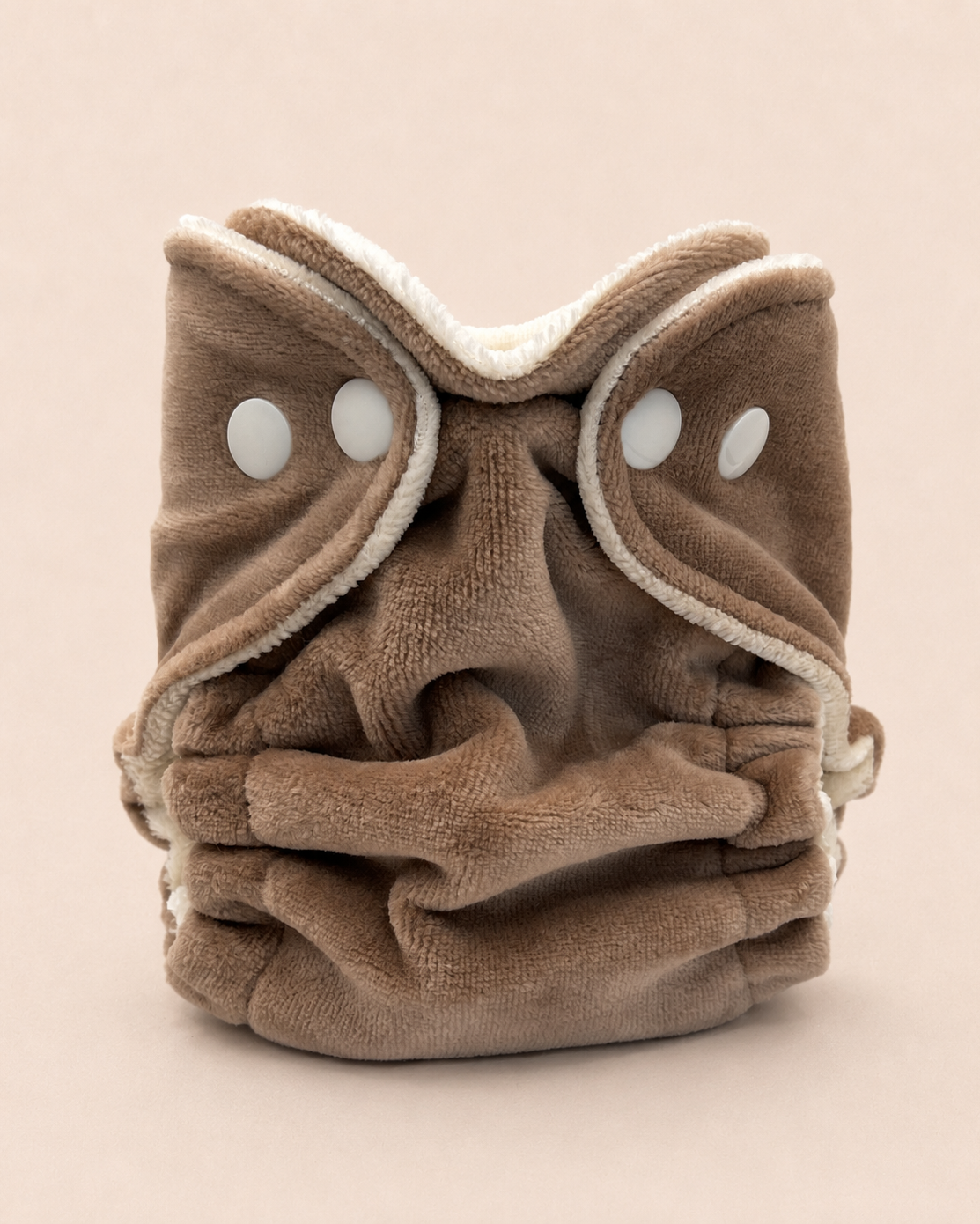 A plush brown cloth face mask with a soft cream fleece trim and two white snap buttons, photographed on a solid light beige background.