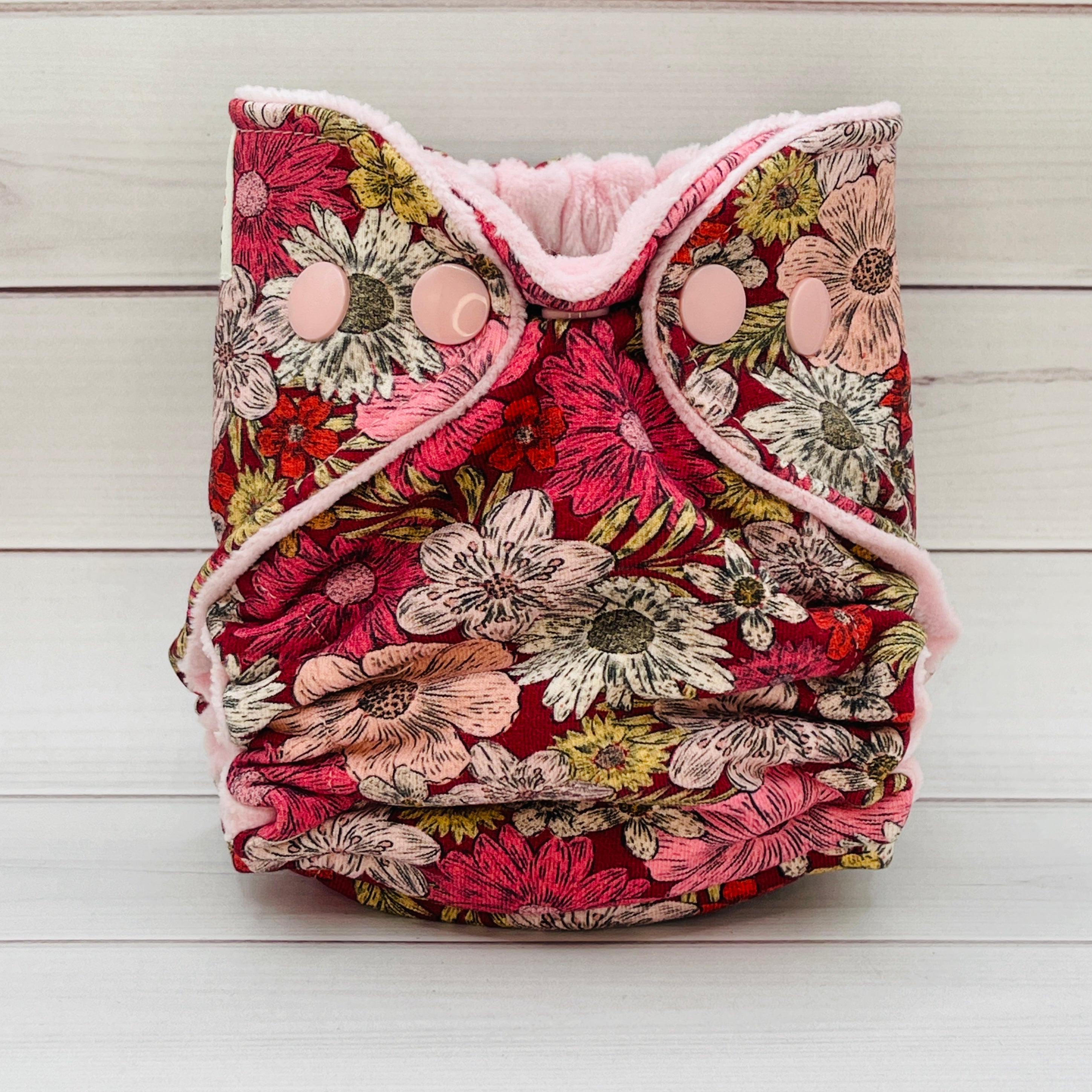 Floral patterned diaper with pink trim on a wooden surface
