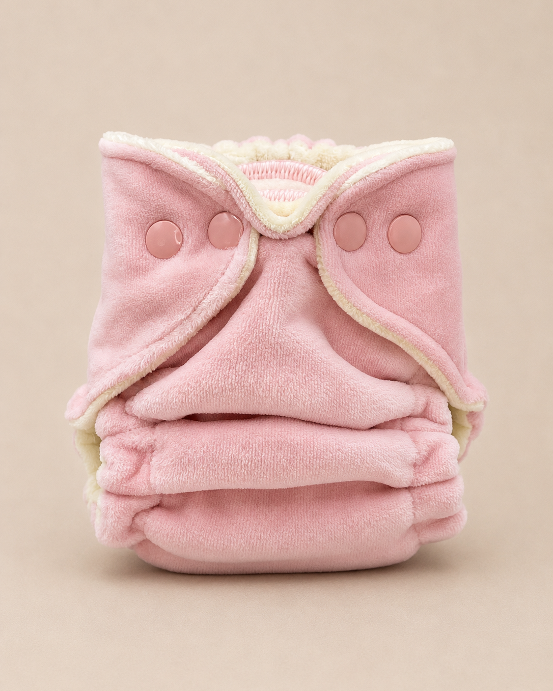 Pink baby cloth diaper with buttons on a beige background