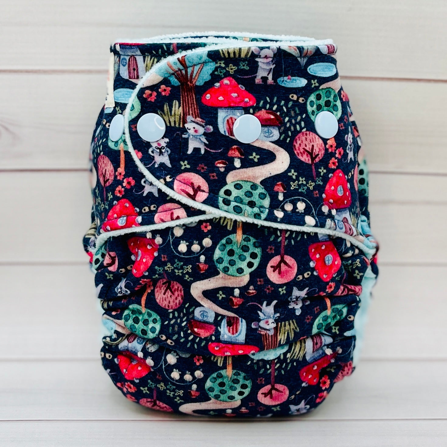 Fitted baby diaper with nature-themed print on a wooden surface