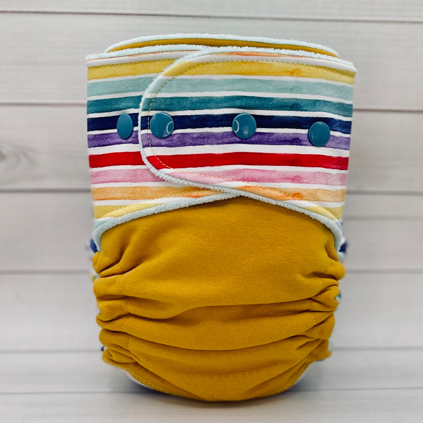 yellow and rainbow striped cloth diaper on a wood table