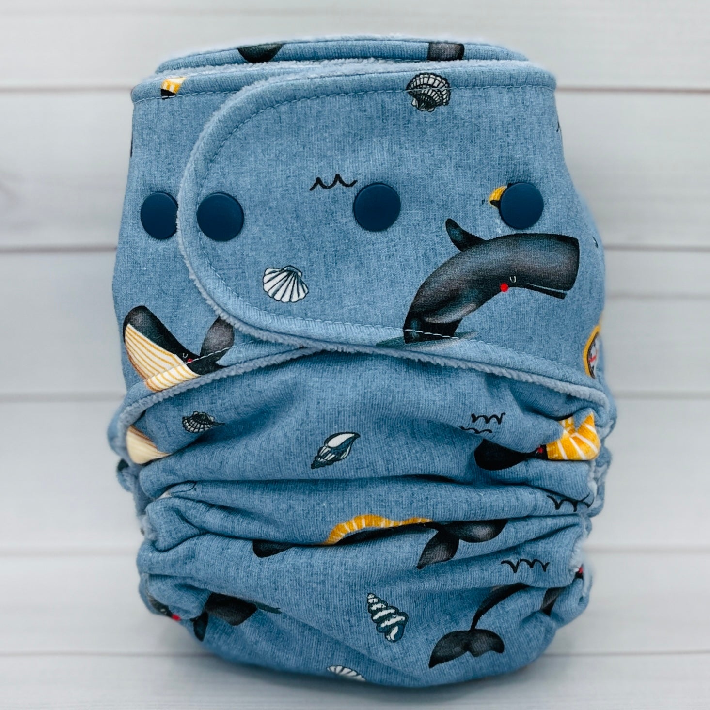 Folded blue fabric diaper with whale pattern on a light wooden background